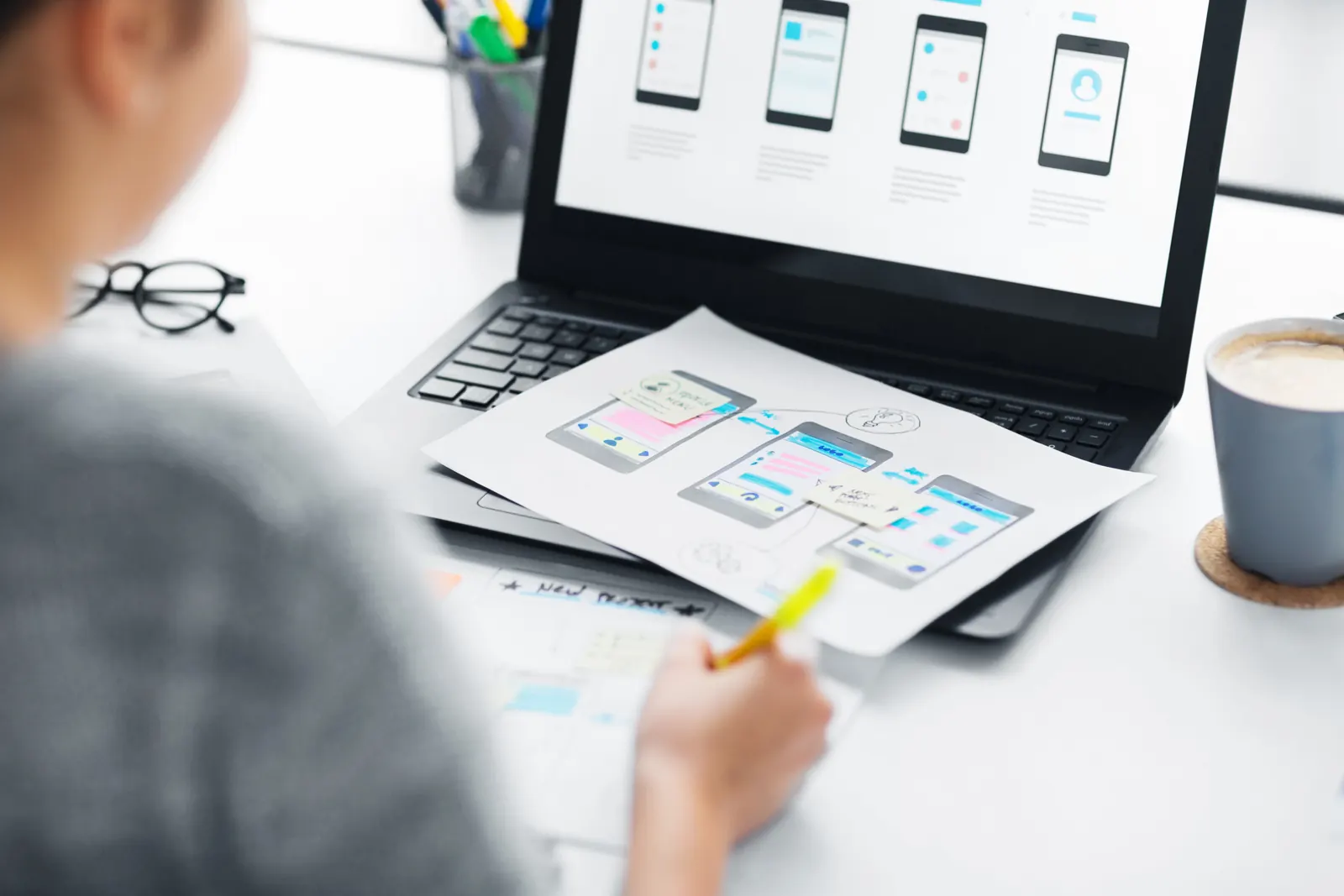 Designer trabalhando nas telas de um portal com rascunhos e notebook